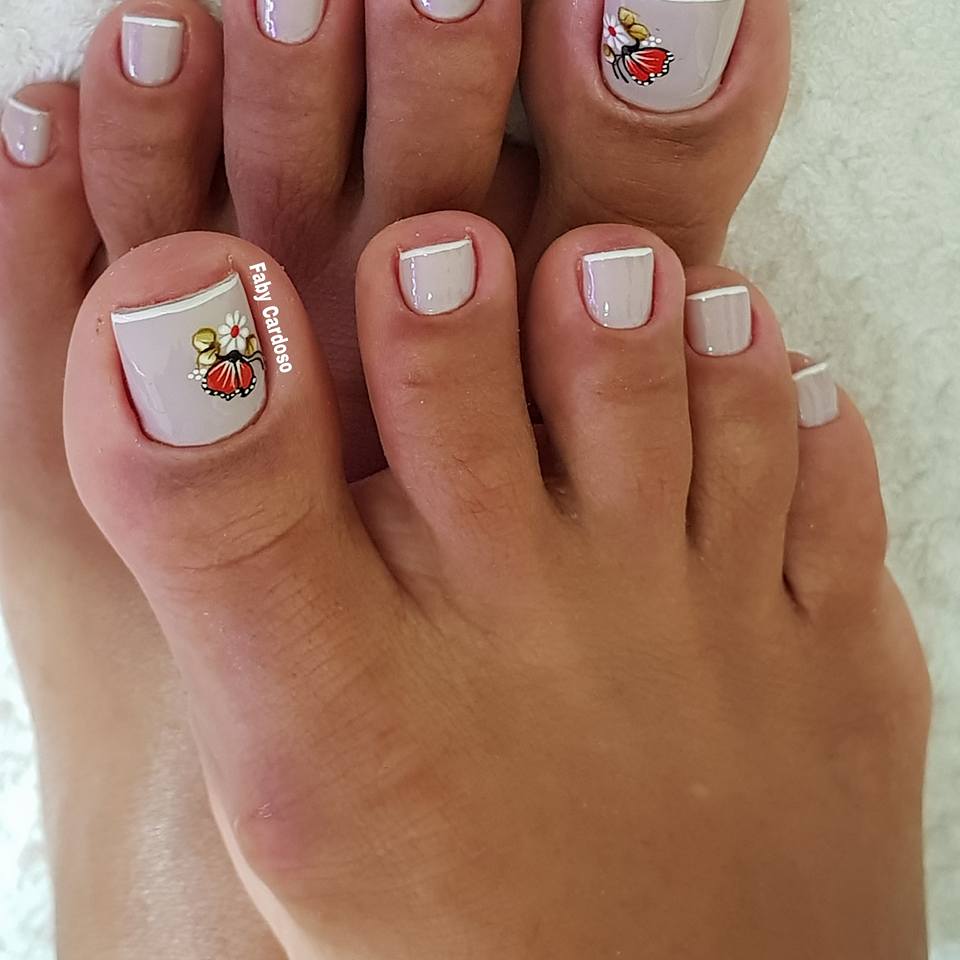 Unhas dos pés pintadas com francesinha esmaltação clara com adesivo no dedão.