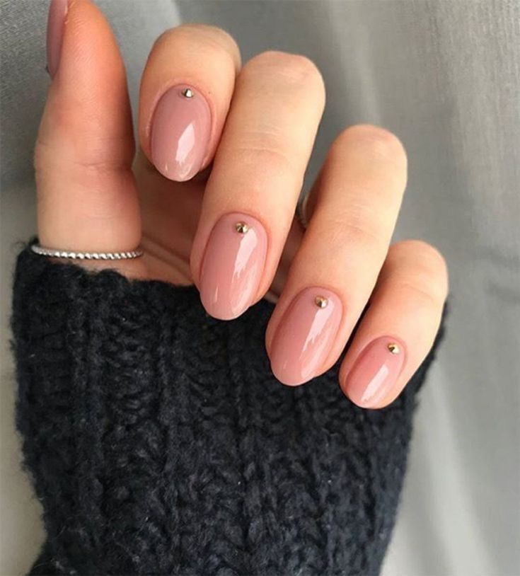 Unhas nude com uma pedraria em cada unha. 