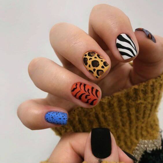 Unhas curtas com cada unha pintada com uma cor e decoração animal print diferente: zebra, onça, tigre.